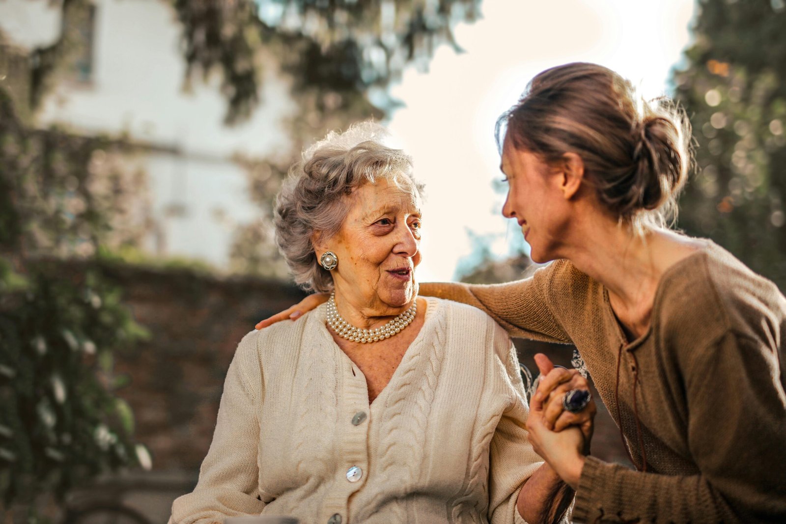 Elderly woman and adult daughter share a joyful, affectionate moment in a sunny garden.