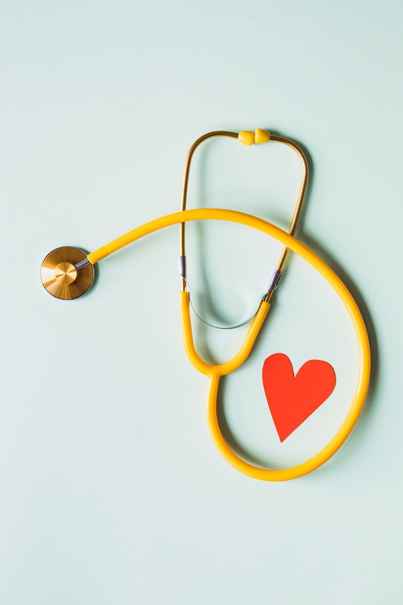 Yellow stethoscope arranged with a red heart cutout on a light green background, symbolizing heart health.